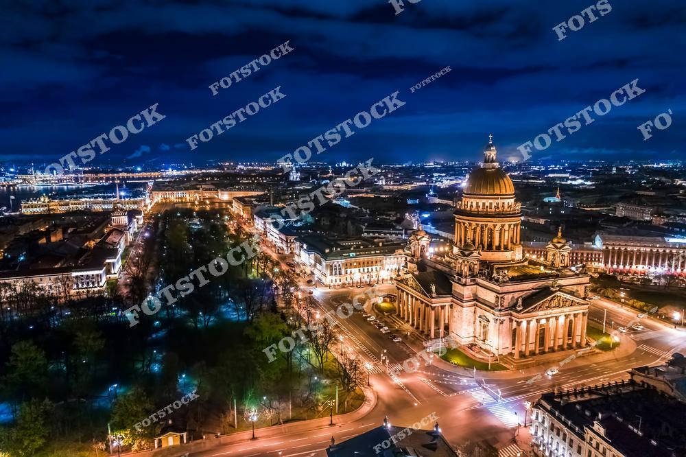 Панорамная фотография центра Санкт-Петербурга ночью, снятая с высоты птичьего полета. На снимке видны Исаакиевский собор, Исаакиевская площадь, улицы города и здания исторического центра. Съемка с дрона позволяет увидеть величие архитектуры, масштабы городской застройки и панораму освещенных улиц. Фотография передает атмосферу ночного Петербурга, красоту городских огней и уникальные панорамные виды культурного и исторического центра. Снимок идеально подходит для туристических публикаций, фотостоков, рекламы, оформления интерьеров и материалов о музеях и достопримечательностях города.